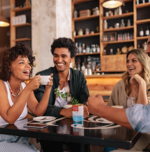 4 people in coffee shop enjoying a coffee and smiling